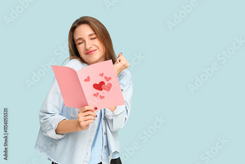 Beautiful young woman holding greeting card with hearts on blue background. Valentine's Day celebration
