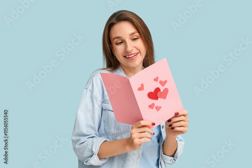 Happy young woman holding greeting card with hearts on blue background. Valentine's Day celebration