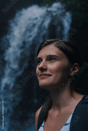 young woman with backpack in front of waterfall smiling at camera photo