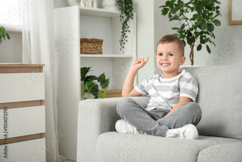 Cute little boy with raised index finger sitting on sofa at home
