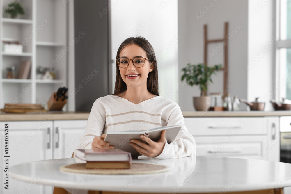 Beautiful young happy woman reading book at table in kitchen Beautiful young happy woman reading book at table in kitchen