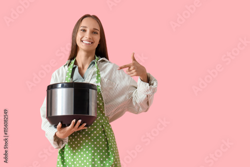 Young housewife pointing at multi cooker on pink background photo