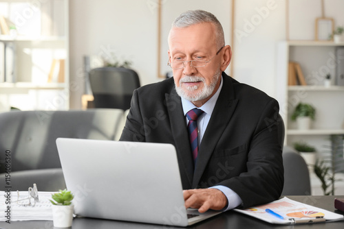 Senior businessman working with laptop at table in office