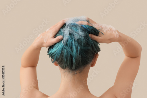 Young woman washing her blue hair on beige background, back view