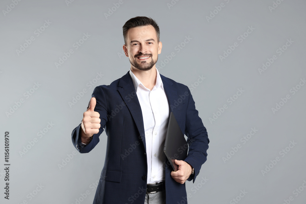 Portrait of smiling banker with laptop showing thumbs up on grey background Portrait of smiling banker with laptop showing thumbs up on grey background