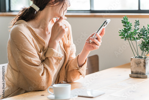 カフェでコーヒーを飲みながらスマホを見る若いアジア人女性（待ち合わせ）
