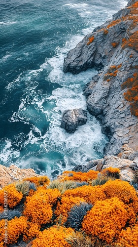 A stunning coastal view featuring vibrant orange flowers cascading over rocky cliffs, contrasting with the deep blue ocean waves crashing against the shore. photo