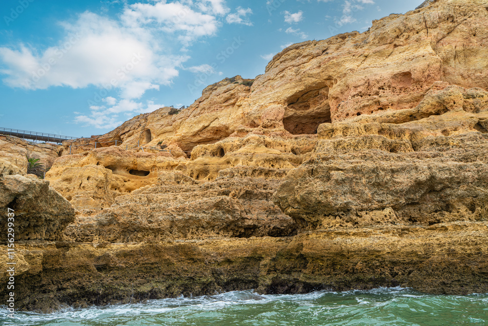 Fototapeta premium At dusk, Golden coastal cliffs rising above emerald waters with intricate sea caves. Features stunning rock formations shaped by waves, Algarve, Portugal.