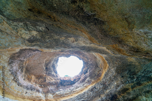 A breathtaking view of the skylight in Benagil Cave, showcasing the natural rock formations and the blue sky above. This famous sea cave is known for its unique beauty. Algarve, Portugal.