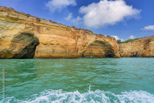 At dusk, Golden coastal cliffs rising above emerald waters with intricate sea caves. Features stunning rock formations shaped by waves, Algarve, Portugal.