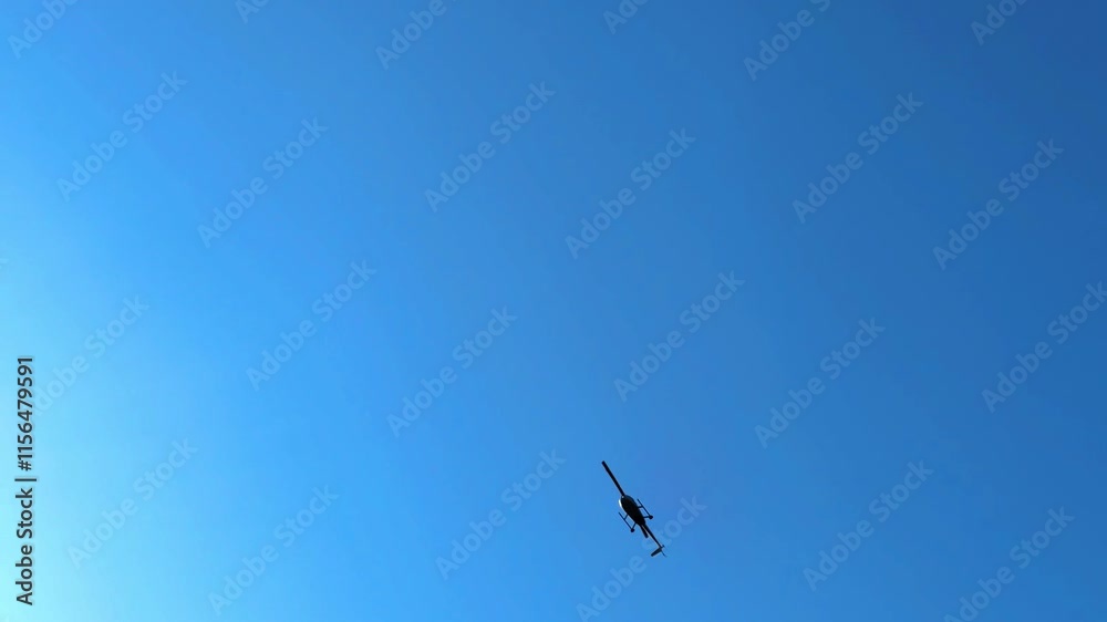 A helicopter overhead flying in the blue sky during the day. A helicopter overhead flying in the blue sky during the day.