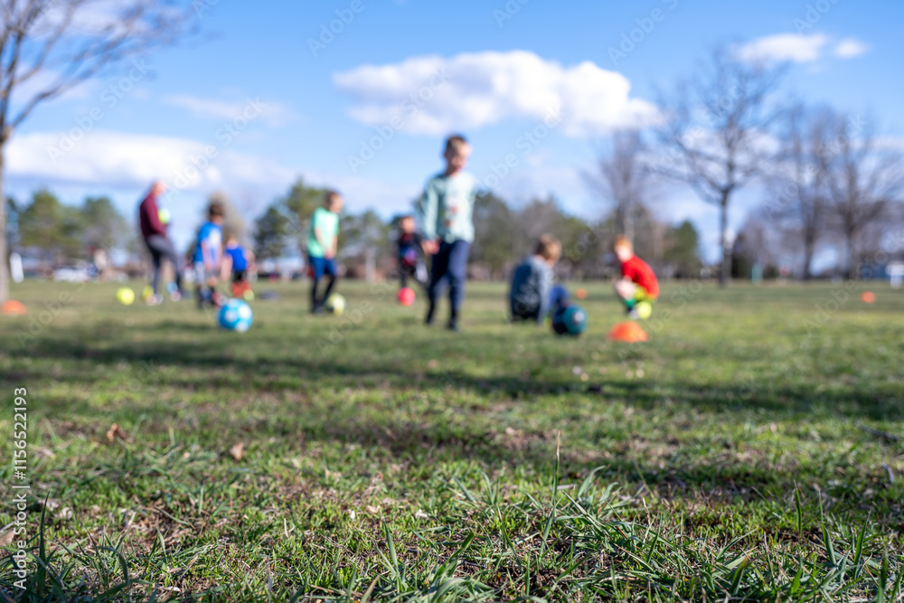 Selective focus on grass with blurred kids soccer practice in the background Selective focus on grass with blurred kids soccer practice in the background