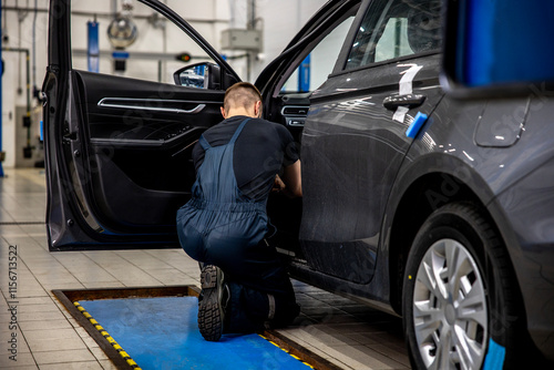 Professional auto mechanic in working uniform repairs electrics in a car