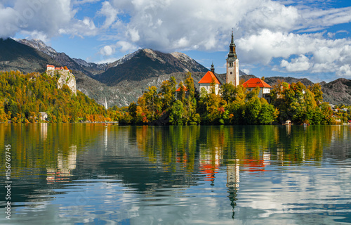 Lake Bled on a sunny autumn day. A view of the island and the Church of the Assumption of Mary. Traveling through Europe, Slovenia. A forest on the cliffs on a sunny day. Tourist attractions of Europe