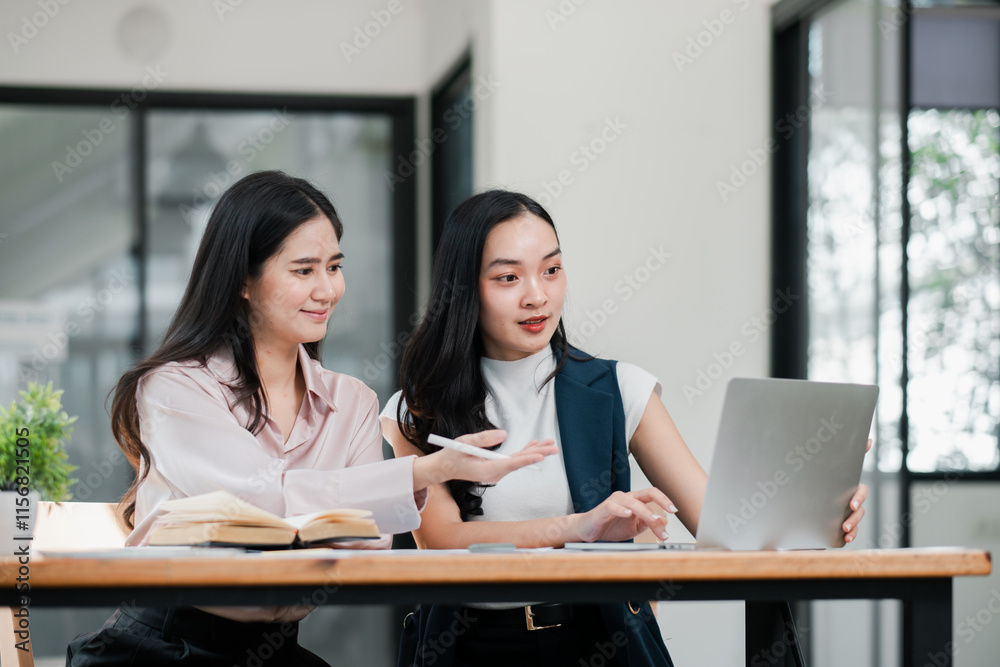 Two businesswomen discussing work at a desk with a laptop, showcasing teamwork and collaboration in a contemporary office environment. Two businesswomen discussing work at a desk with a laptop, showcasing teamwork and collaboration in a contemporary office environment.