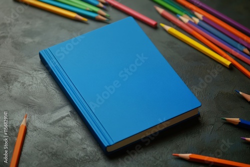 A plain blue notebook for a children's book mockup. Notebook surrounded by colored pencils
