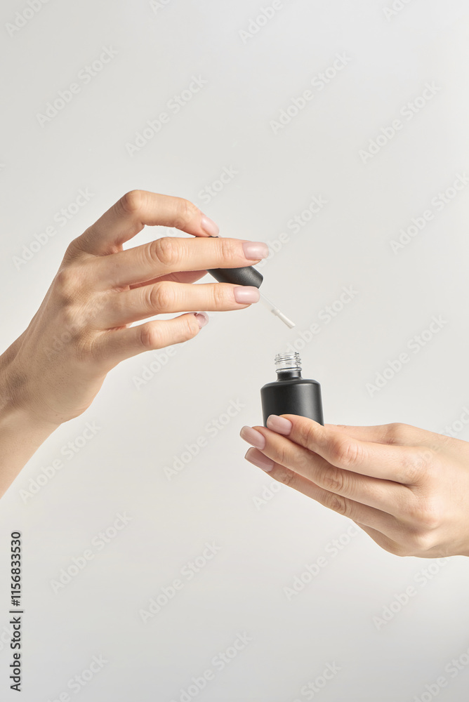 Hands holding a bottle of nail polish with an open cap ready for application in a minimalist setting Hands holding a bottle of nail polish with an open cap ready for application in a minimalist setting