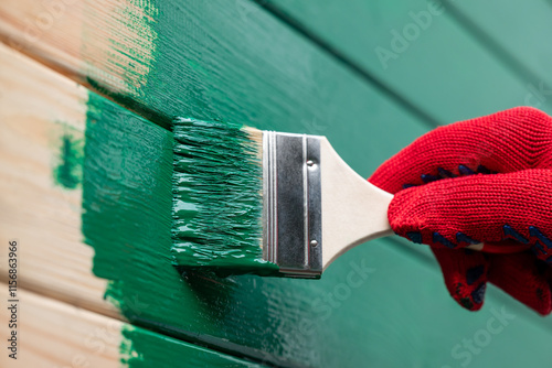 Painting outdoor house wall with a brush. Man painting wooden wall in green color, renovating house, new facade