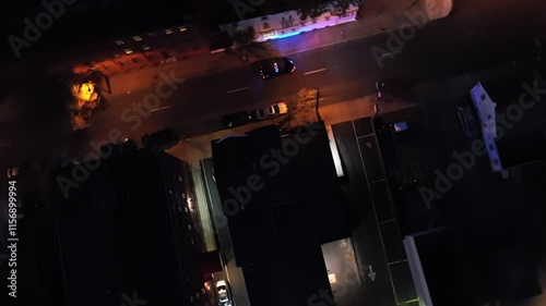 Blinking blue and red lights of police car driving on street at night. Orange lighting lantern along Main Street of city. Tracking drone shot.