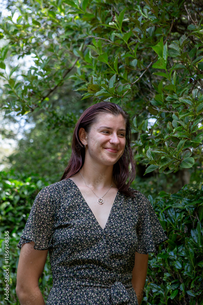 A smiling woman in a floral dress stands outdoors in front of stone steps surrounded by lush greenery. The natural light and vibrant backdrop enhance the cheerful and serene atmosphere A smiling woman in a floral dress stands outdoors in front of stone steps surrounded by lush greenery. The natural light and vibrant backdrop enhance the cheerful and serene atmosphere