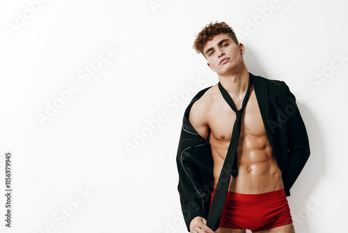 Confident young man posing dramatically in red swimwear, wearing an unbuttoned jacket and loosely tied tie. Fashion and style concept. photo