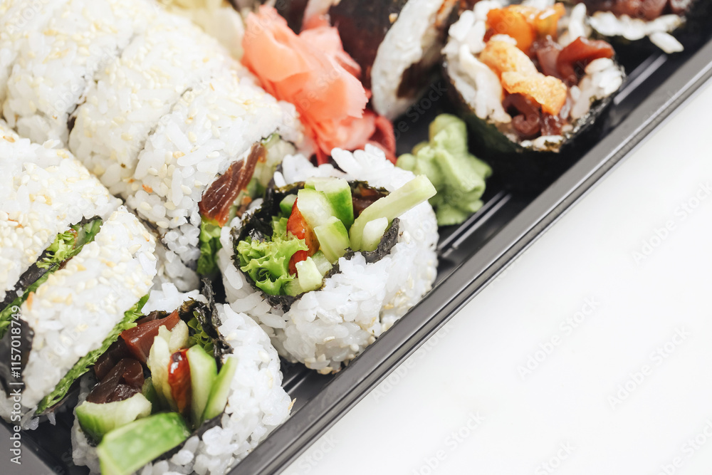 Sushi assortment in a black takeaway box. Closeup of California rolls, futomaki, and uramaki. Fresh Japanese cuisine with sesame seeds and colorful toppings. Lunch or dinner sushi to-go option. Sushi assortment in a black takeaway box. Closeup of California rolls, futomaki, and uramaki. Fresh Japanese cuisine with sesame seeds and colorful toppings. Lunch or dinner sushi to-go option.
