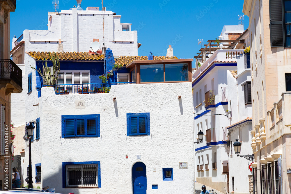 Delivery man riding a scooter in a narrow street with white houses in sitges, spain