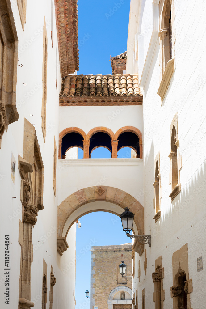 Delivery man riding a scooter in a narrow street with white houses in sitges, spain