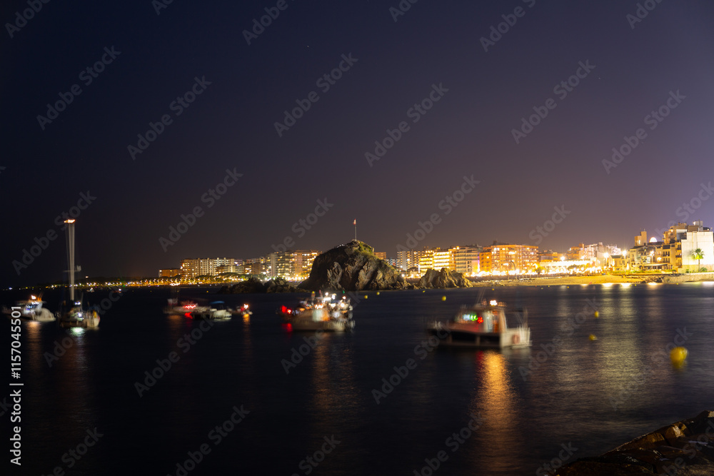 People relaxing on beach at night, watching summer festival with illuminated buildings in background