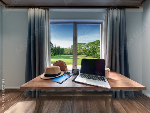 A wooden desk sits before a large window overlooking a lush green landscape.  A laptop, hat, camera, and notebook are arranged on the desk, suggesting work and travel. photo