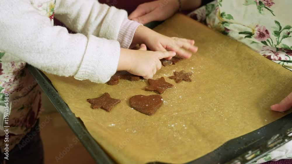 Child and mother making christmas cookies together, arranging star and heart shaped gingerbread cookies on a baking tray Child and mother making christmas cookies together, arranging star and heart shaped gingerbread cookies on a baking tray