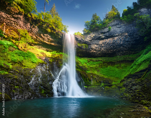 Majestic waterfall cascading down a lush green cliff into a river below, surrounded by vibrant foliage and a clear blue sky