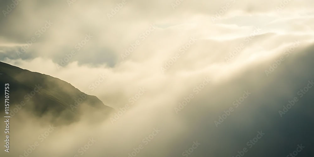 Obraz premium Misty mountain peak shrouded in fog, sunlight breaking through clouds.