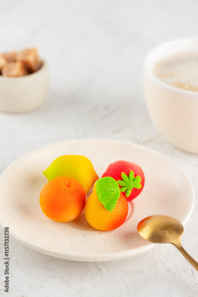 Marzipan candies in the form of fruits: pear, tangerine, lemon and strawberry in a plate with a cup of coffee on the table. Vertical orientation. Marzipan candies in the form of fruits: pear, tangerine, lemon and strawberry in a plate with a cup of coffee on the table. Vertical orientation.