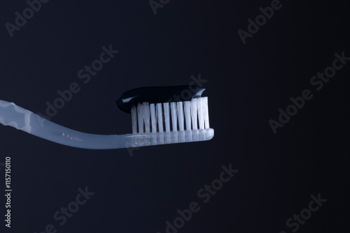 Black toothpaste on a White toothbrush with White bristles close-up on a black background