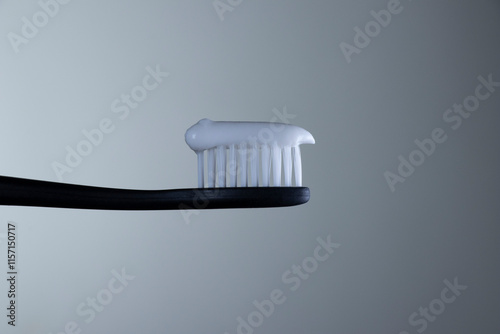 White toothpaste on a black toothbrush with white bristles close-up on a gradient gray background