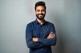 Confident Indian businessman stands in studio portrait. Successful entrepreneur corporate executive wears navy blue shirt. Beard. Arms crossed. Isolated against neutral gray background. Posing