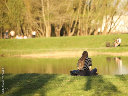 A young girl meditates on the river bank sitting on green grass. Peace of mind and emotional balance. Relaxing alone in nature. Achieving Mental Health
