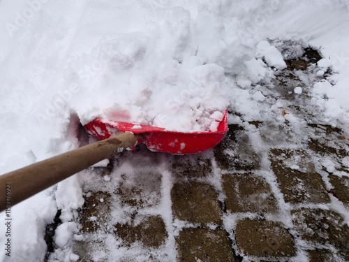 Clearing snow from the sidewalk with a red plastic shovel in winter. Cleaning snow-covered areas.