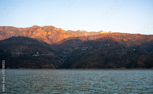 The scene captures the blue mountains above the lake during the golden hour, with calm waters mirroring the stunning landscape in Tehri Lake. photo