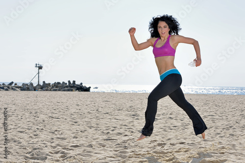 Attractive brunette woman works out on beach - wearing pink sports bra - holding a water bottle bounds across sand photo