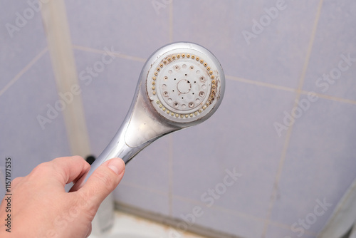 hand holding a silver shower head with limescales that should be cleaned. Calcified shower due to hard water. Calcium mineral buildup.