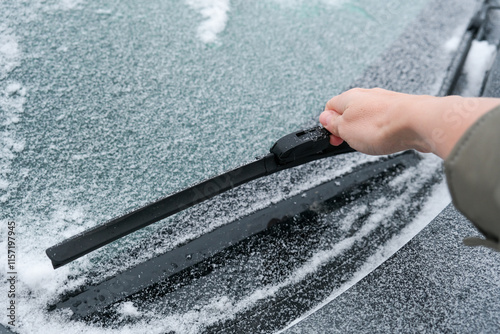 Hand trying to clean car wiper blades. Flakes of snow covered the car with a thick layer. Safe driving with working wipers and clean windshield.