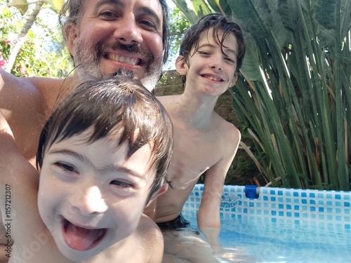 Padre e hijos  uno con síndrome Down, se divierten al al aire libre en pileta de lona jugando