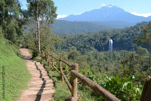 A peaceful hiking trail leading to a scenic waterfall, surrounded by lush greenery and dappled sunlight
