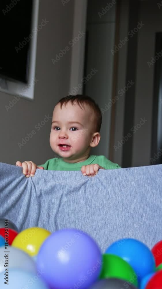 Active Caucasian baby boy playing near the dry pool filled with balls. Kid jumps up holding by the basin edge. Vertical video Active Caucasian baby boy playing near the dry pool filled with balls. Kid jumps up holding by the basin edge. Vertical video