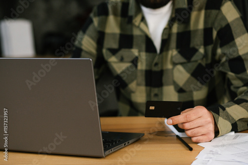 Close up of man hand holding black credit card and using laptop, shopping online, doing secure payment. Internet banking concept.