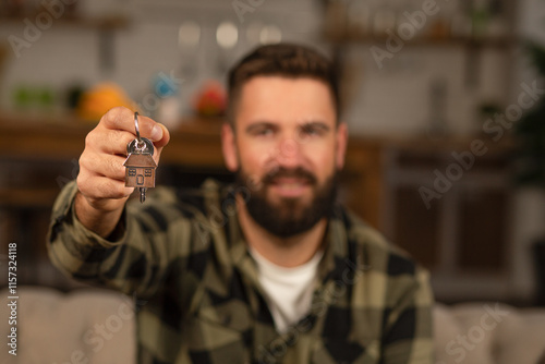 Smiling handsome man holding a house-shaped keychain, keys at home, real estate concept