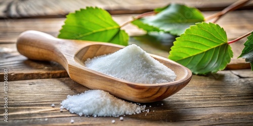 Close-up of scoop filled with xylitol sugar substitute next to birch sugar, leaves, and wood, xylitol photo