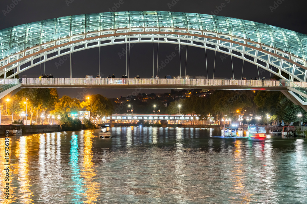 Night view of the illuminated pedestrian bridge over the river in Tbilisi with reflections and city lights Night view of the illuminated pedestrian bridge over the river in Tbilisi with reflections and city lights